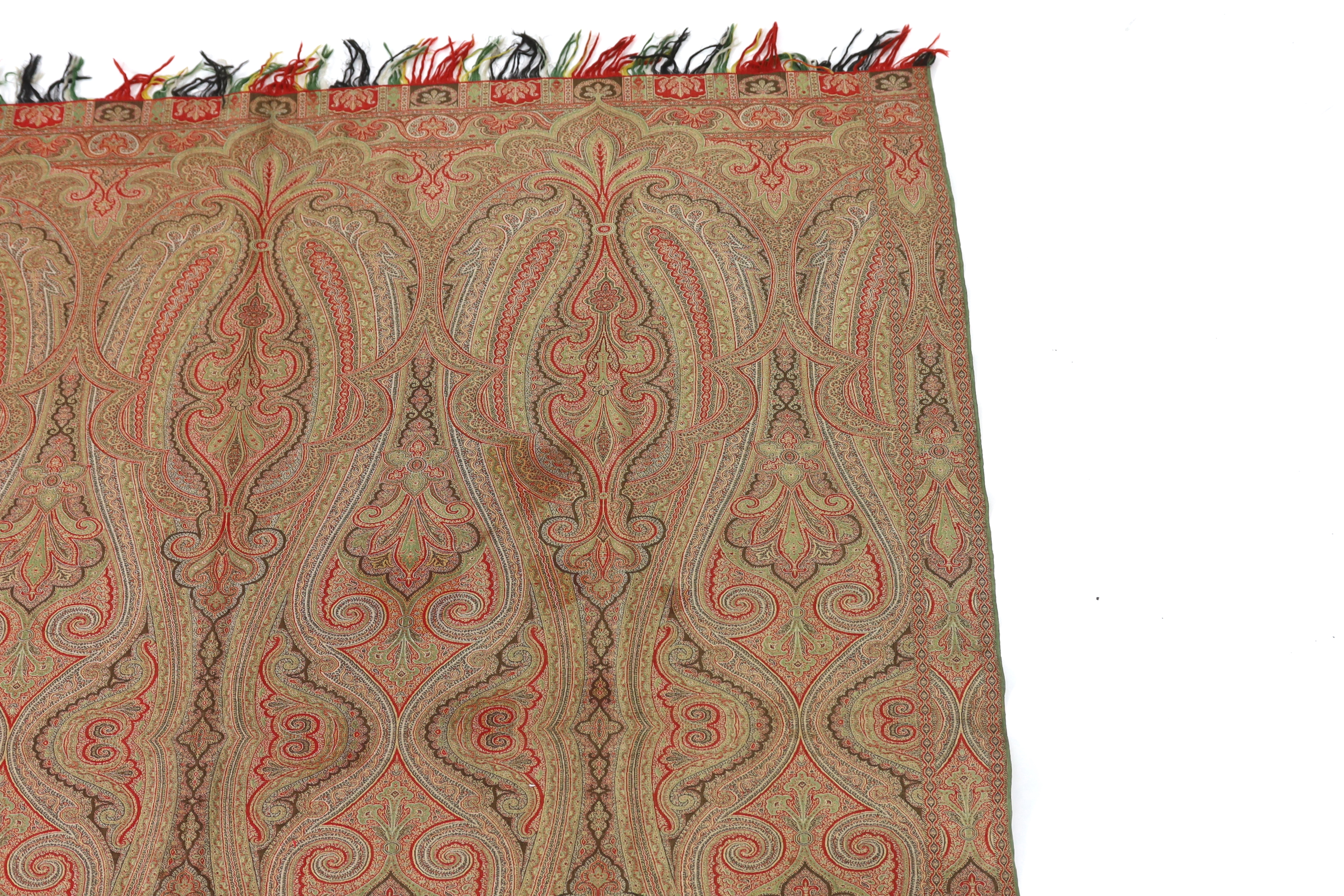 An 1860’s, reversible woven wool Paisley shawl, woven with green, red, ochre and brown, with a woven border and fringing both ends. 166cm wide x 169cm long